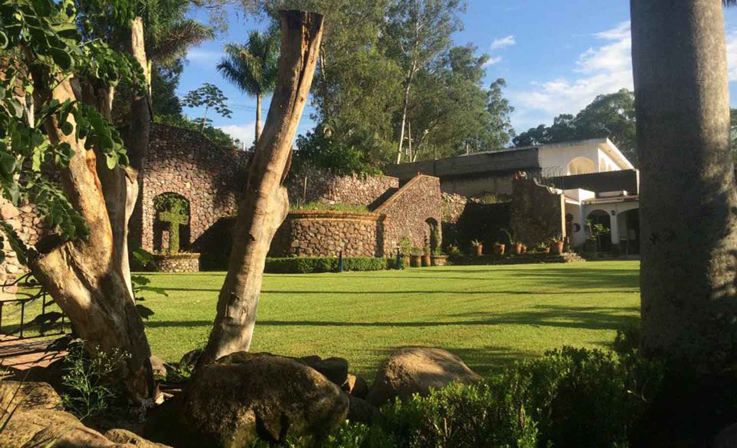 Jardín de gran tamaño con árboles y, al fondo, un edificio de arquitectura de estilo tradicional.