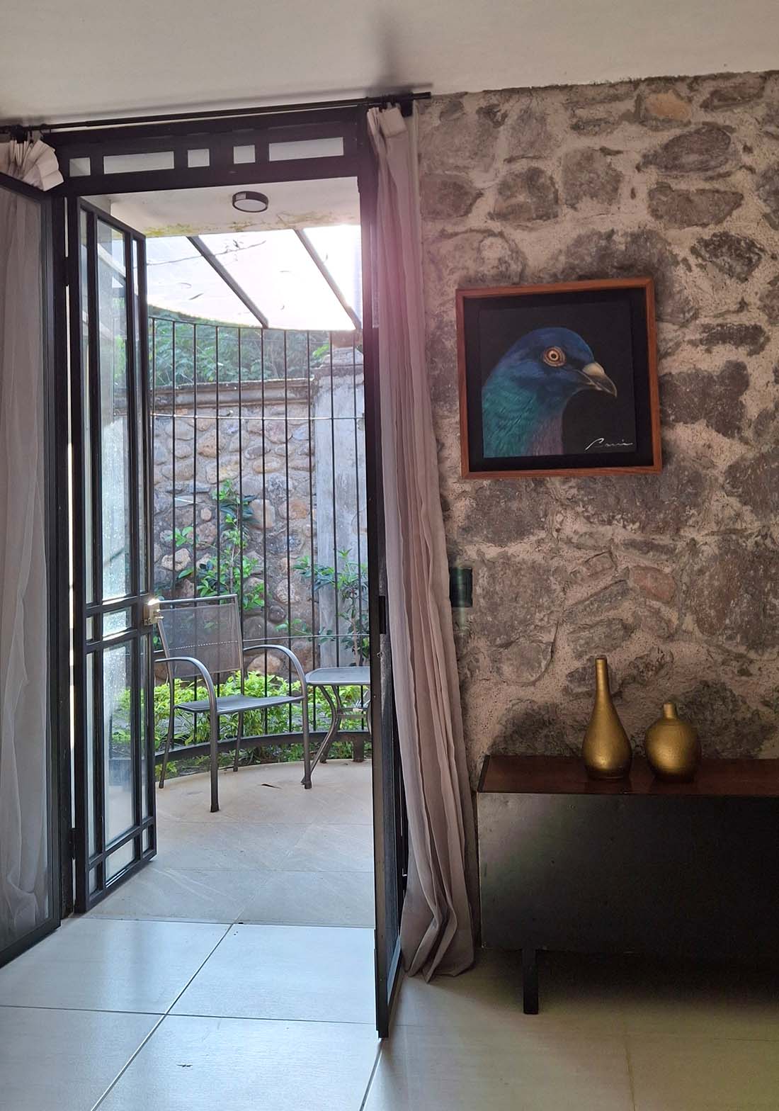 Interior de una habitación de la hotelería Quinta Pichón, estilo tradicional con acabados de mampostería en algunas paredes y un balcón con jardinerías y sillas.