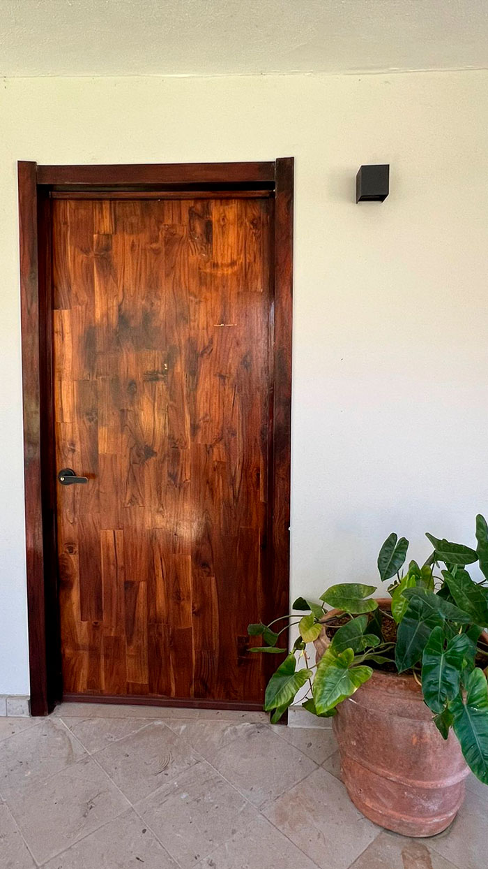 Entrada de una habitación de la hotelería Quinta Pichón; tiene una pared blanca y puerta de madera estilo tradicional.