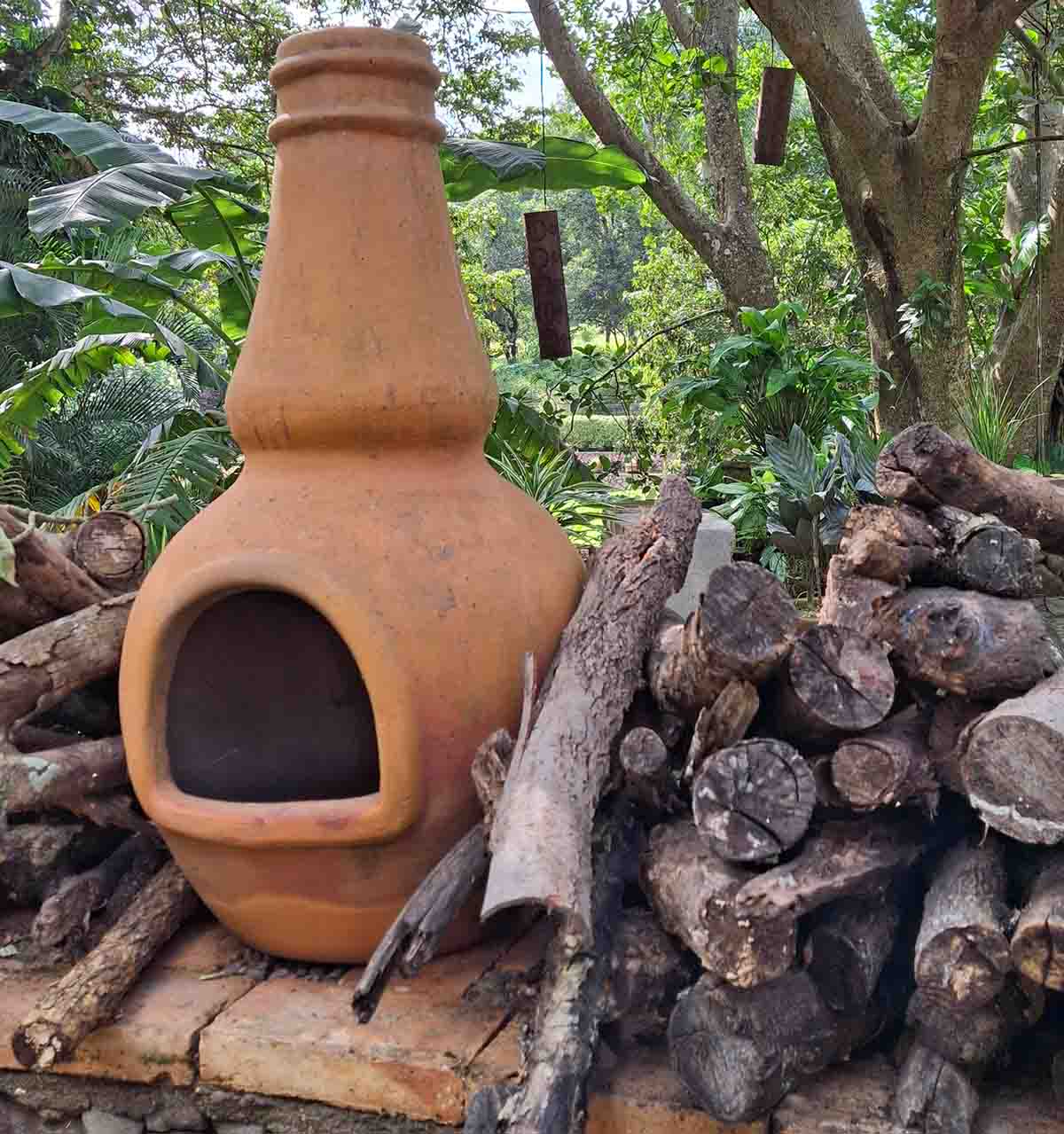 Chimenea mexicana de barro con leña a un costado de ellas situadas en un jardín.