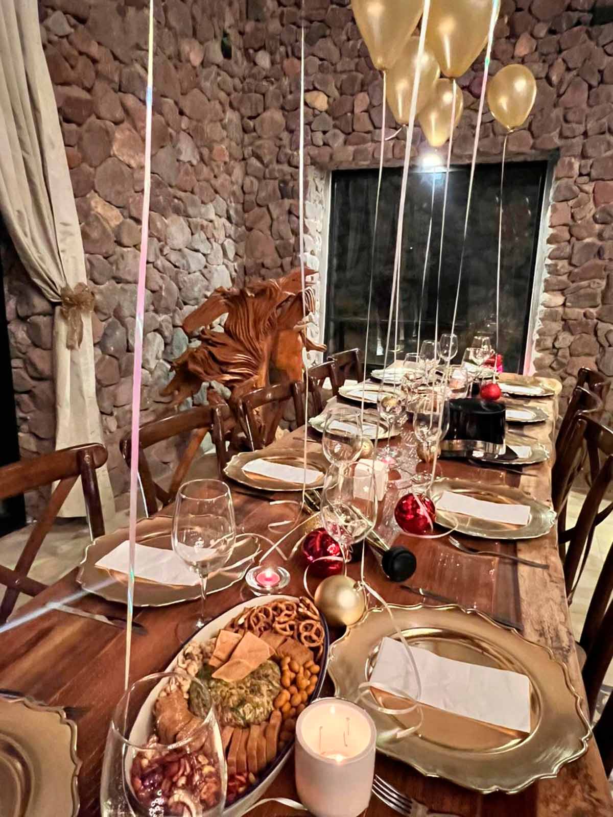 Interior de uno de los edificios de Quinta Pichón, donde se celebra un evento social, con una gran mesa de madera al centro, decorada con platos, cubiertos y globos.