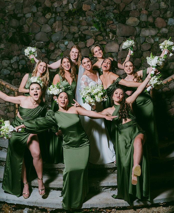 Sesión fotográfica de una novia con sus damas de compañía; la novia viste de blanco y las damas de compañía con vestidos color verde. La sesión fue echa en una sección de Quinta Pichón en Nayarit, con una arquitectura rústica.