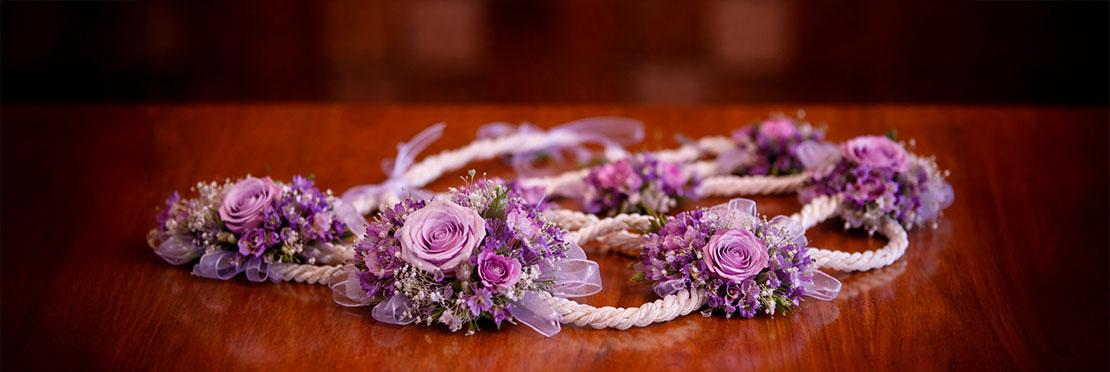 Lazo de color blanco adornado con flores de color morado y violeta esta situado encima de una mesa de madera.