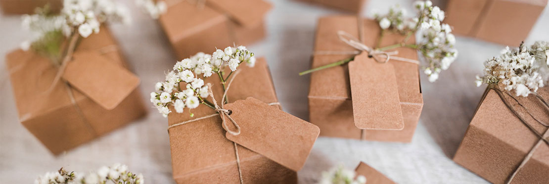 Regalos forrados con papel de tipo cartón y atados con un lazo y adornados con flores pequeñas color blanco.