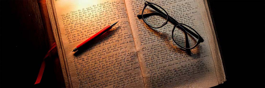 hoja de papel en la cual fue escrito un texto amano y sobre el papel hay un bolígrafo de color rojo y un unos anteojos.