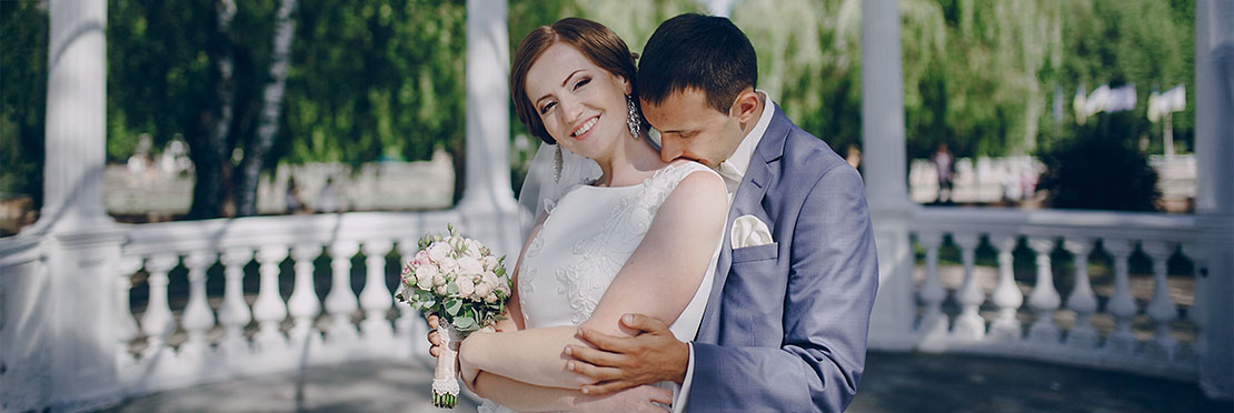 Pareja de novios abrazados el esta besando su cuello y ella sonríe muestra mucha felicidad.